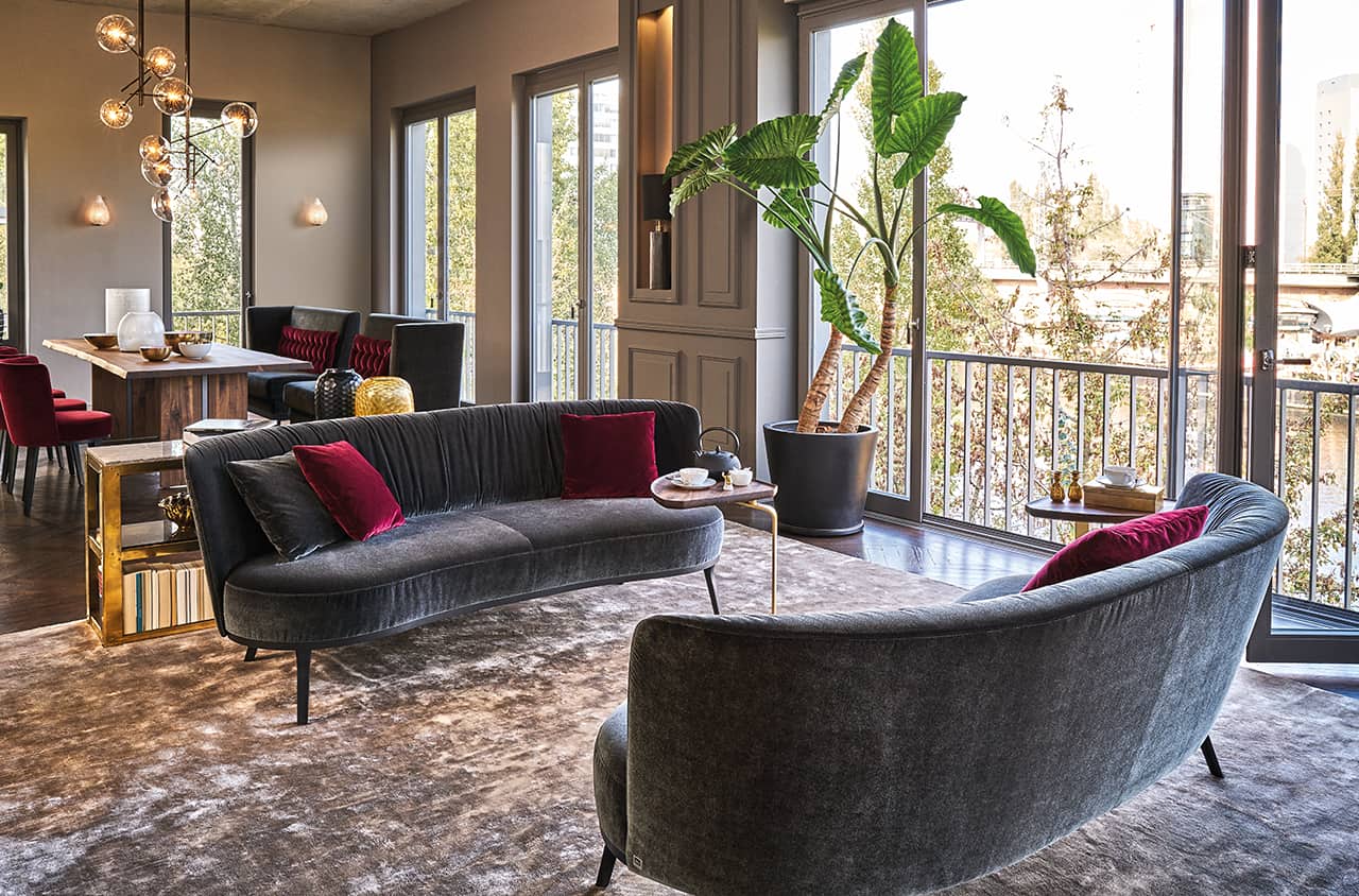 Geschwungenes Sofa in dunklem Stoff mit eleganter, warmer Ausstrahlung.